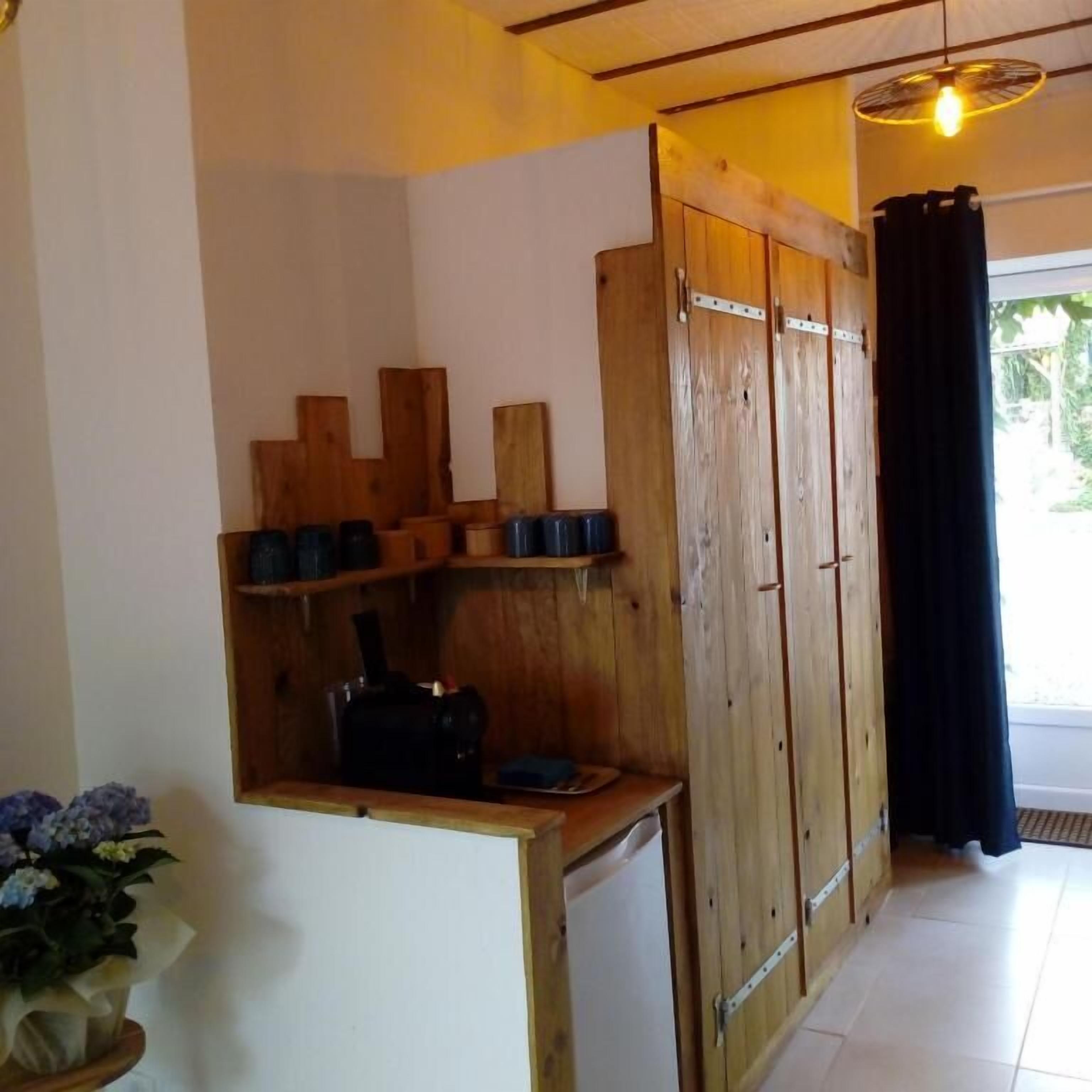 A room with wooden cabinets, a small shelf with cups, a potted plant, and a window with a curtain.