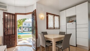 Eine Küche mit Esstisch, Stühlen, einem Kühlschrank und einem Fenster mit Vorhängen.