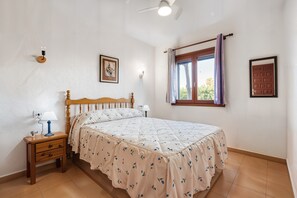 Ein Schlafzimmer mit Bett, Nachttisch, Lampe, Wandleuchte, Fenster mit Vorhängen und einer Tür.