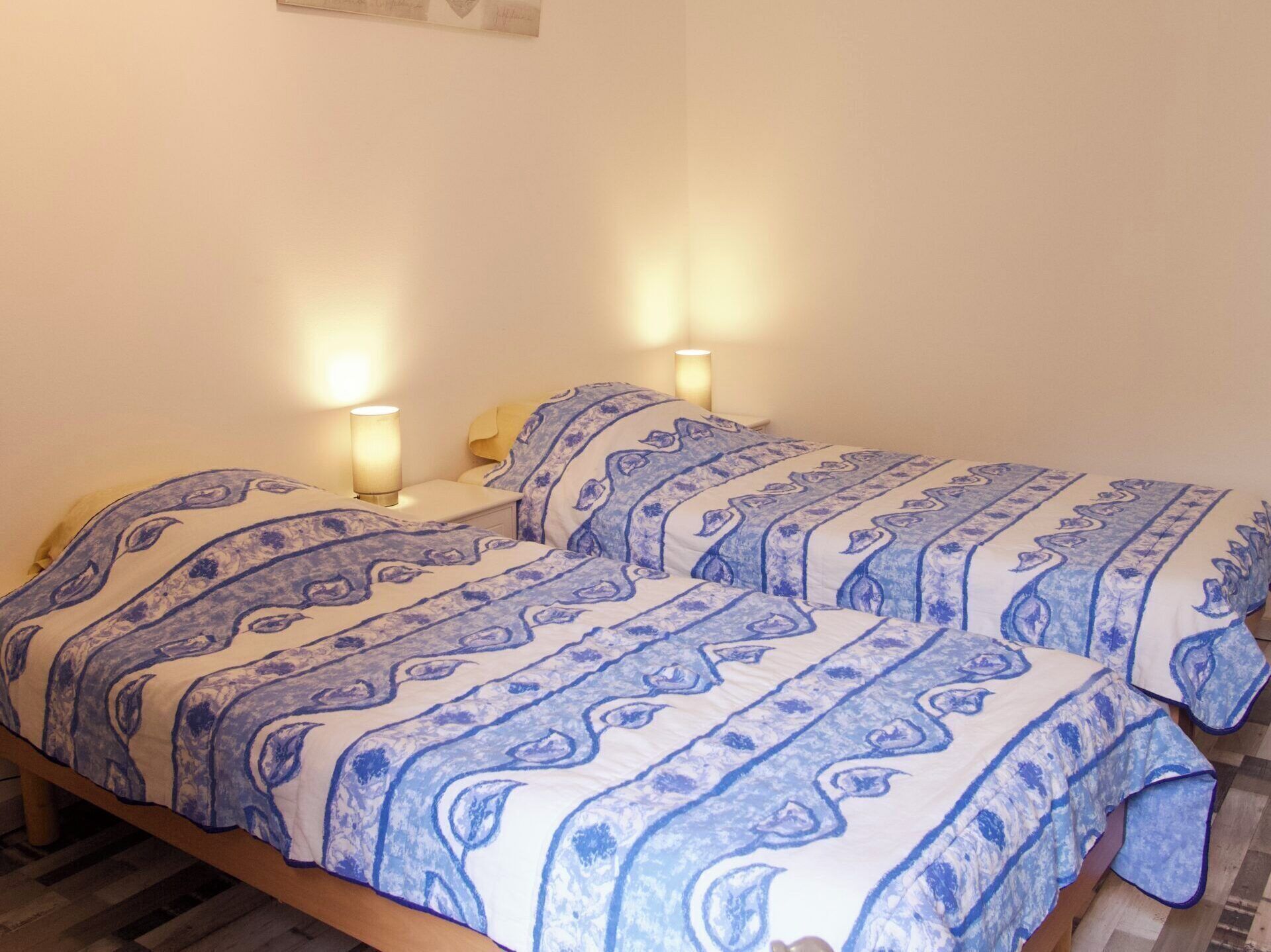 En dubbelsäng med mönstrat sänglinne, två sänglampor och en sänggavel i trä.
