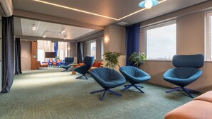 Una habitación de hotel moderna con un ventanal grande, un televisor de pantalla plana y una zona de estar con sillas azules.