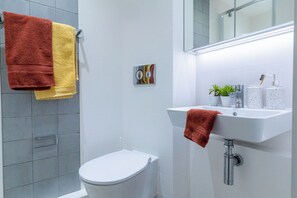 Une salle de bain moderne avec des toilettes blanches, un lavabo avec une serviette et un espace douche.