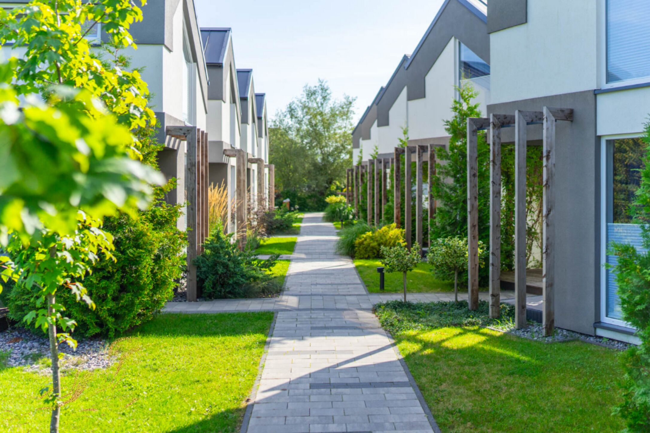 En modern bostadsbyggnad med en stenlagd gångväg, grönska och träpergola.
