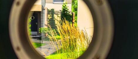 A view through a circular opening, revealing a building with a modern design, a door, and some grass in the foreground.