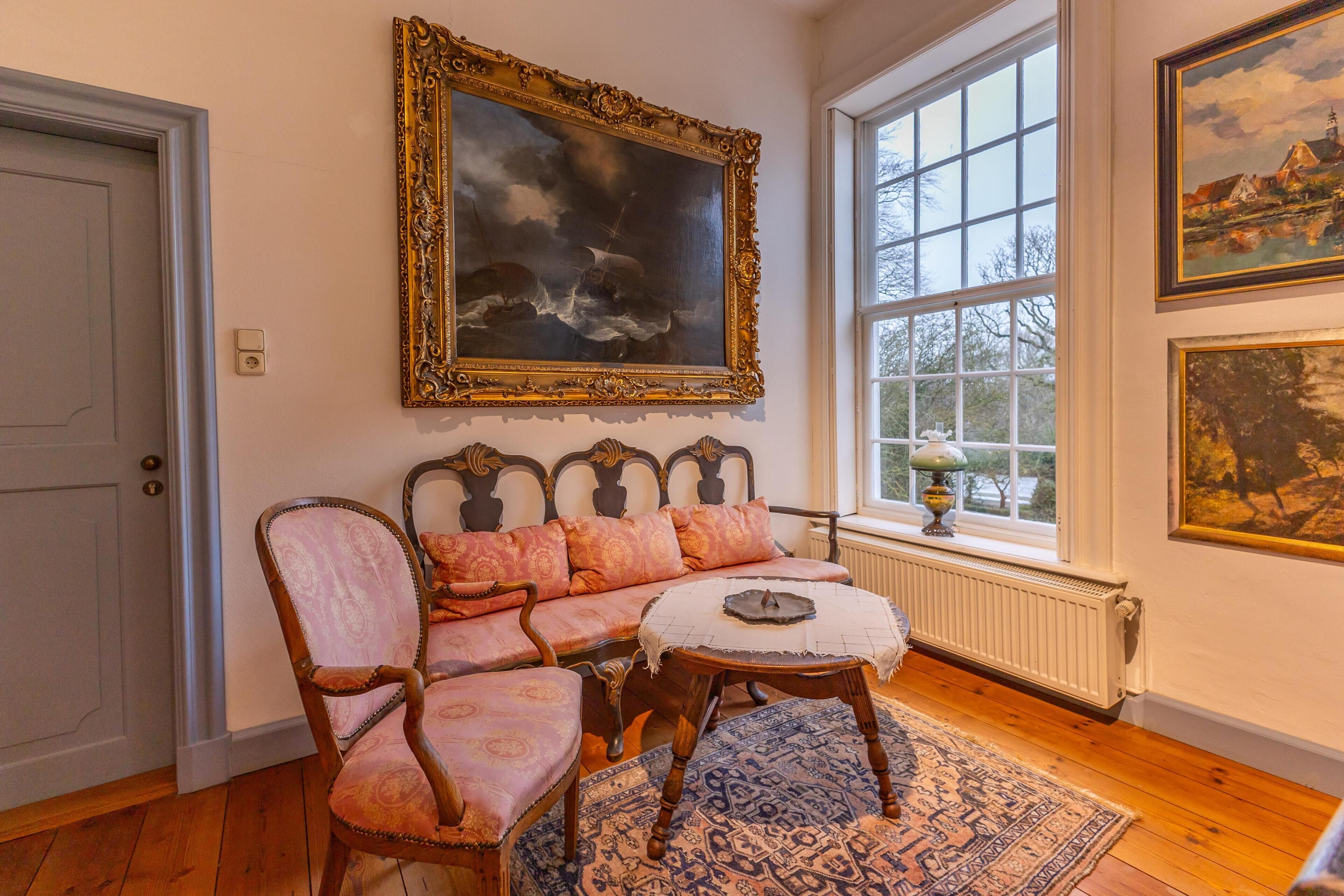 Une pièce avec un plancher en bois, un canapé agrémenté de coussins à motifs, une table ronde et un grand tableau encadré au-dessus du canapé.