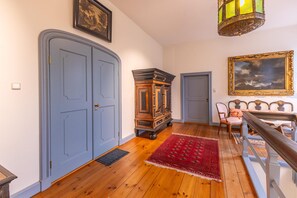 A hallway with wooden flooring, a red rug, a vintage wooden cabinet, and a dining area with chairs and a table. - Vacation apartment "Ukena" - Stately living in the Harlem house (Krummhörn)