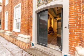 A brick building with a dark entrance door, white window frames, and a small step leading to the door. - Vacation apartment "Ukena" - Stately living in the Harlem house (Krummhörn)