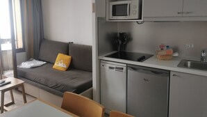 A compact kitchen with a microwave, sink, and dishwasher. A gray sofa with a yellow pillow is in the living area. - Avoriaz 1800 Apartment 4/5 p (Morzine)