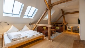 A loft-style bedroom with a wooden bed, a desk, and a sofa. There are skylights and a TV mounted on the wall. - Vacation apartment "Attena" - Living above the rooftops of Greetsiel (Krummhörn)