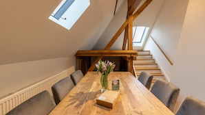 A dining area with a wooden table, six chairs, a vase with flowers, and a staircase with wooden beams. - Vacation apartment "Attena" - Living above the rooftops of Greetsiel (Krummhörn)