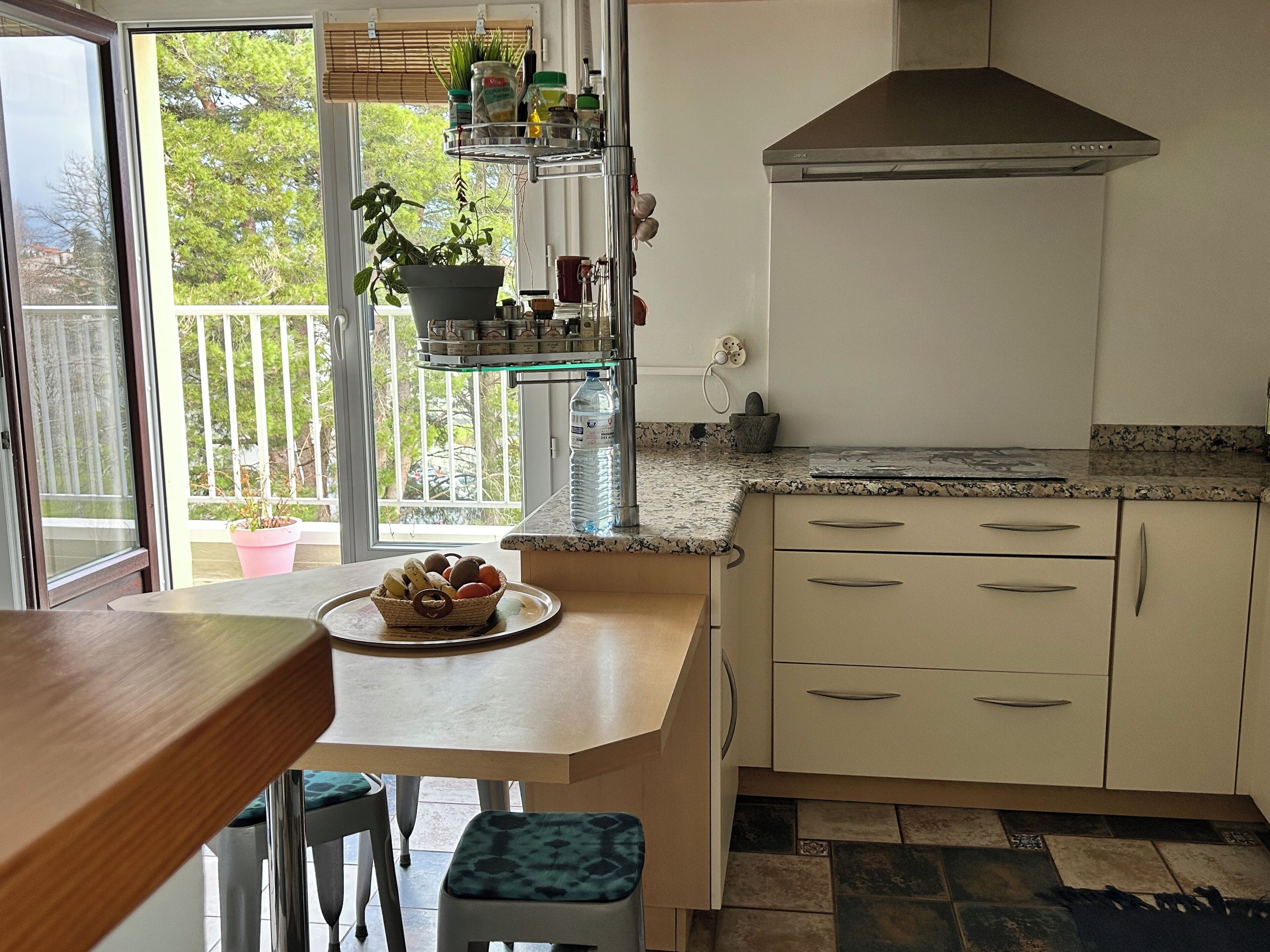 A kitchen with a wooden table, a sink, a stove, and a window with a view of trees.