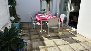 Una terrazza con tavolo apparecchiato per mangiare, sedie, piante in vaso e una porta scorrevole in vetro che dà su uno spazio esterno.