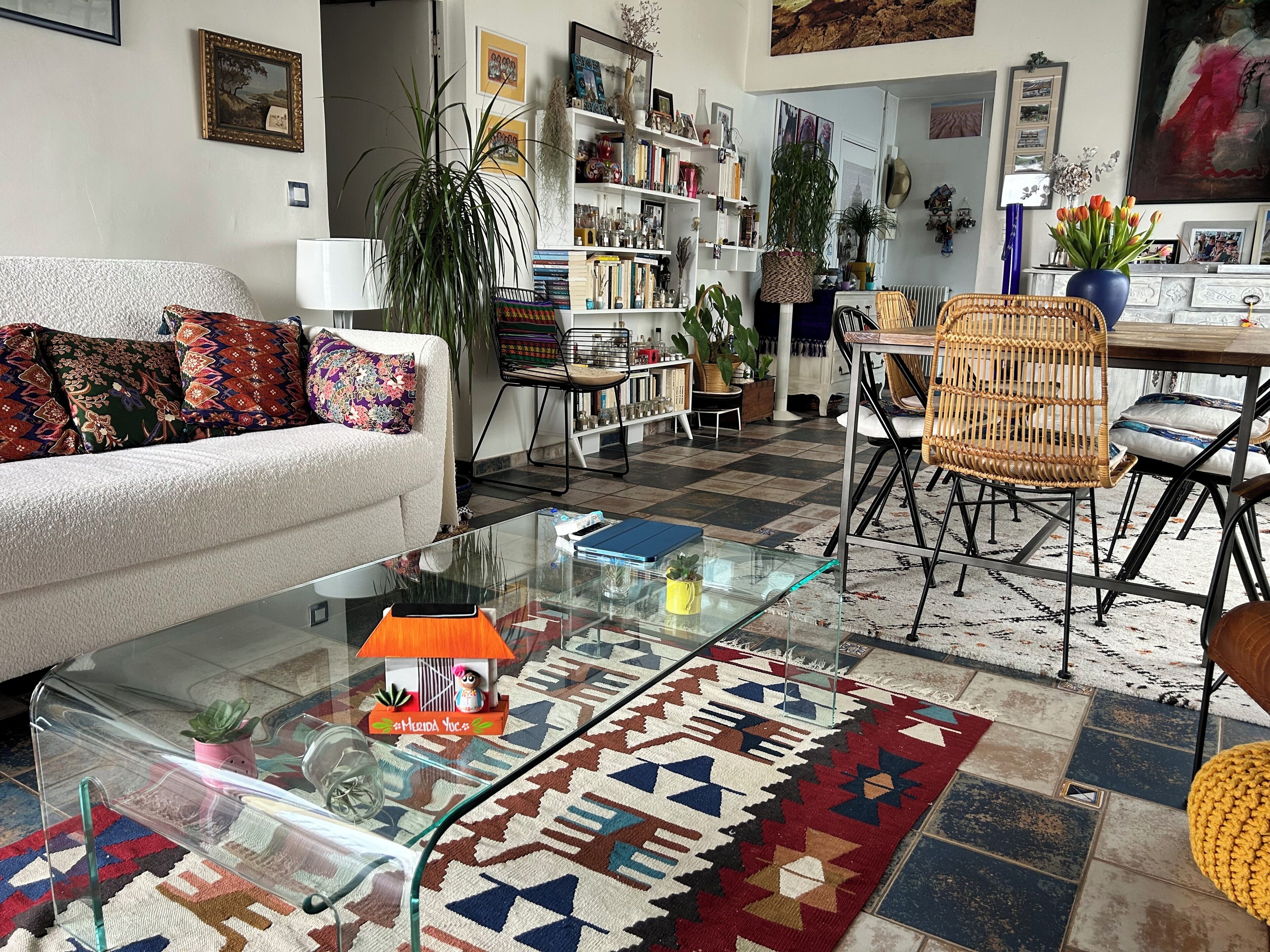 A living room with a sofa, coffee table, and chairs, a bookshelf, and a patterned rug.