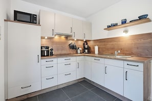 A modern kitchen with white cabinets, a microwave, a coffee maker, and a wooden backsplash. - Modern Cordula vacation apartment with garden, terrace and e-charging station (Greetsiel)