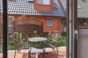A patio with a round table and two chairs, a wooden gate, and a brick building with a tiled roof. - Cordula: A Modern Vacation Apartment with a Garden, Terrace, and Electric Charging Station (Greetsiel)