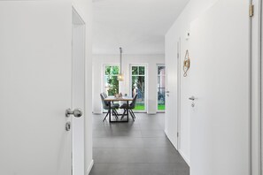 Ein Flur, der in einen Essbereich mit Tisch und Stühlen führt, mit einer Hängeleuchte und einer Tür mit Schlüsselloch.