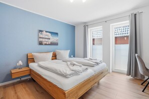 A bedroom with a bed, a nightstand, a lamp, a window with curtains, and a picture on the wall. - Cordula: A Modern Vacation Apartment with a Garden, Terrace, and Electric Charging Station (Greetsiel)