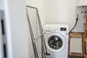 Ein kleiner Waschbereich mit einer Frontlademaschine, einem Wäscheständer und einem kleinen Holzschrank.
