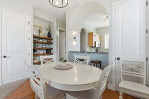 A dining area with a round table and white chairs, a white door, and a kitchen visible through an archway. - Stone Cliff Oasis Scenic Views (Branson)