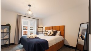 Quarto bem arrumado com cama, mesa de cabeceira, espelho e janela com cortinas.