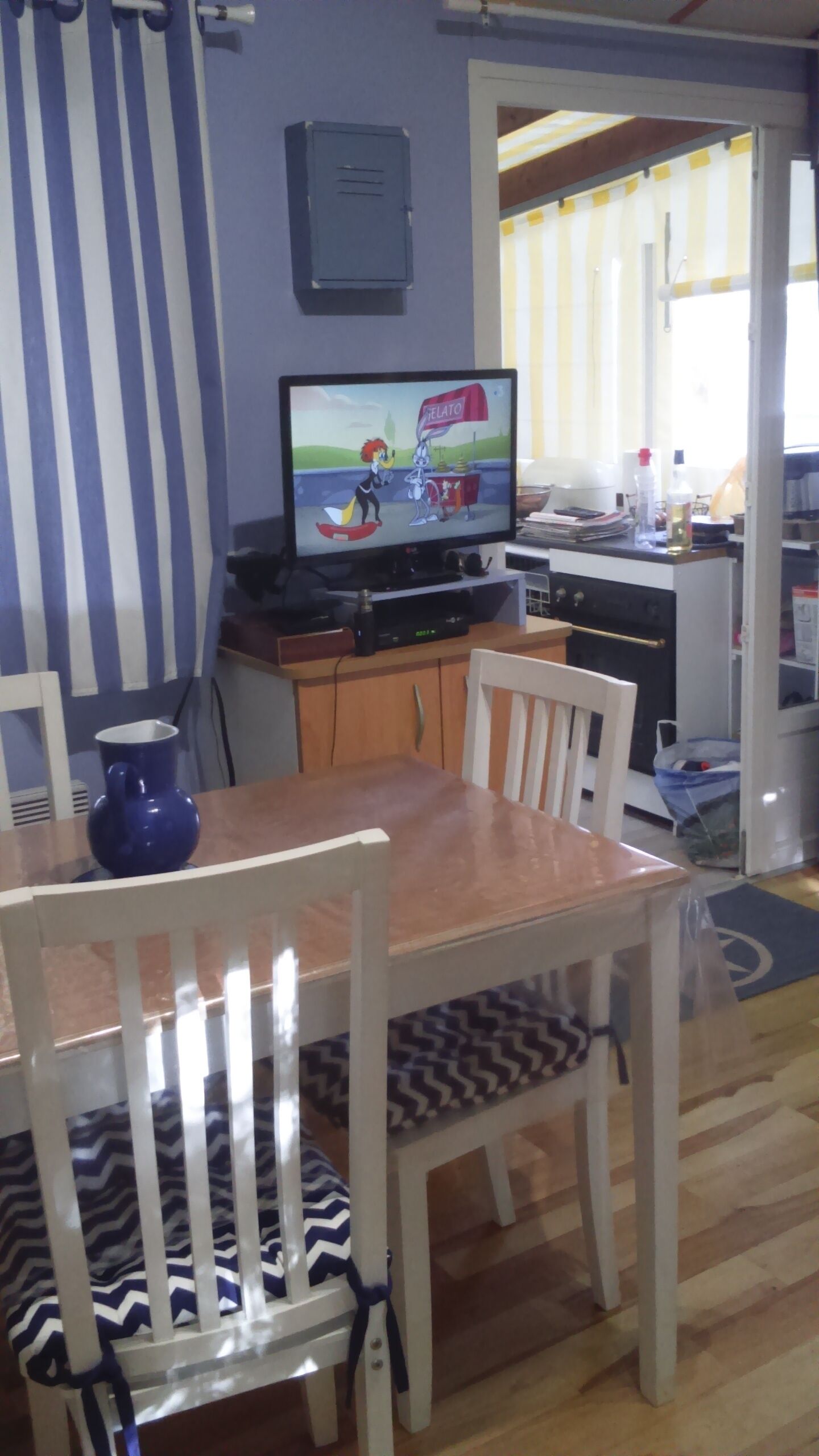 Een eetgedeelte met een tafel, stoelen, een televisie en een keuken op de achtergrond.