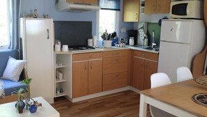 A compact kitchen with wooden cabinets, a microwave, a refrigerator, and a dining area with a table and chairs. - Seasonal rental fully equipped mobile home for 4/6 people (Saint-Hilaire-de-Riez)