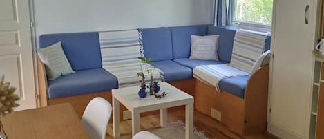 A cozy living area with a blue sofa, a small table with decorative items, a white cabinet, and a window with curtains.