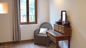 Ein Zimmer mit einem Holztisch, einem Korbstuhl und einem Fenster mit Vorhängen.