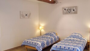Ein Zimmer mit zwei Einzelbetten, Holzboden, einer Wandlampe und einem Bild mit Herz und Blumen.