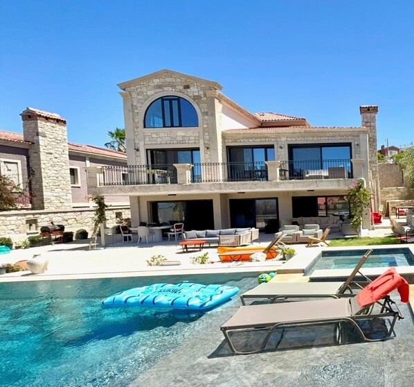 A two-story house with a swimming pool, outdoor furniture, and a patio area.