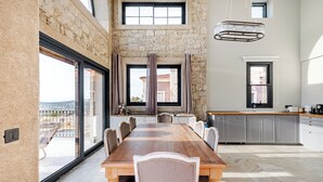 A spacious dining area with a large wooden table and chairs, a stone wall, and a view of the outdoors.
