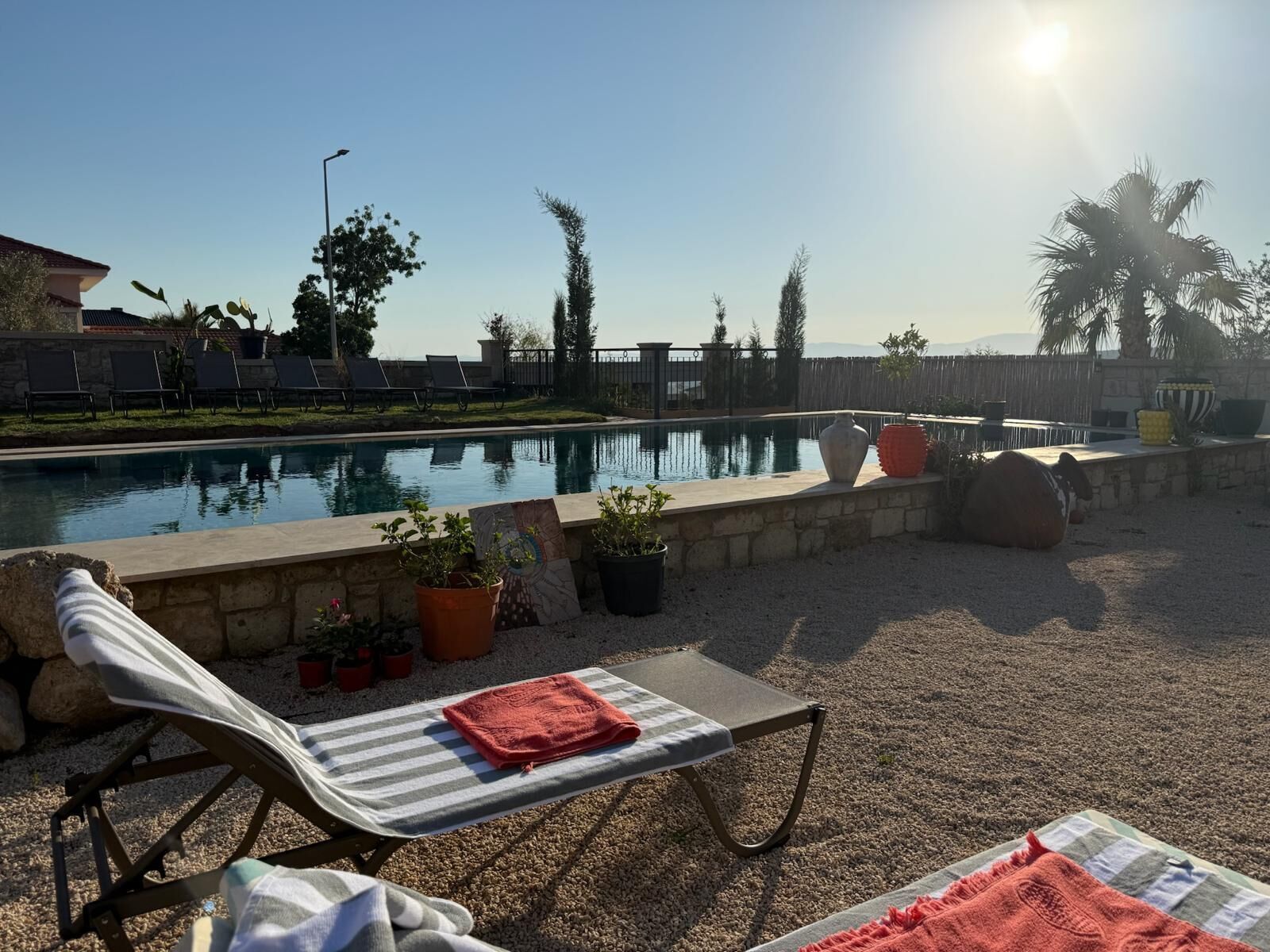 Un espace aménagé au bord de la piscine, avec des chaises longues, une petite table et une serviette, ainsi que des plantes en pot.