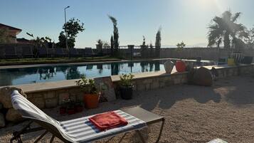 Un espace aménagé au bord de la piscine, avec des chaises longues, une petite table et une serviette, ainsi que des plantes en pot.