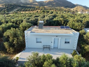 Un bâtiment blanc doté d’un toit plat, de panneaux solaires et d’une petite table sur le porche avant.
