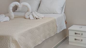 A neatly made bed with a quilted cover, a heart-shaped towel decoration, and a white bedside table with drawers.