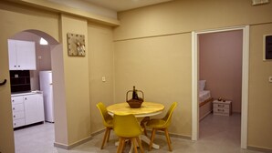 Un espace de vie compact comprenant un coin repas avec une table ronde et quatre chaises jaunes, un coin cuisine et une chambre avec un lit et une table de chevet.