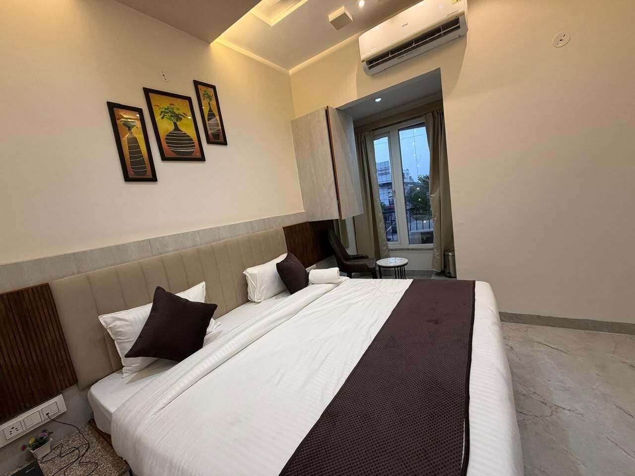 Habitación de hotel con una cama grande, cabecera, ventana y cuadros en la pared.