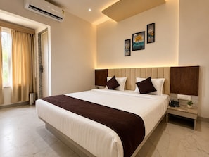 Habitación de hotel con una cama grande, una mesita de noche, aire acondicionado instalado en la pared y una ventana con cortinas.