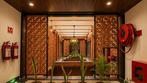 A reception area with a wooden reception desk, potted plants, a fire hose reel, and fire extinguishers. - Hotel Maniratna Premium (Sanwer)
