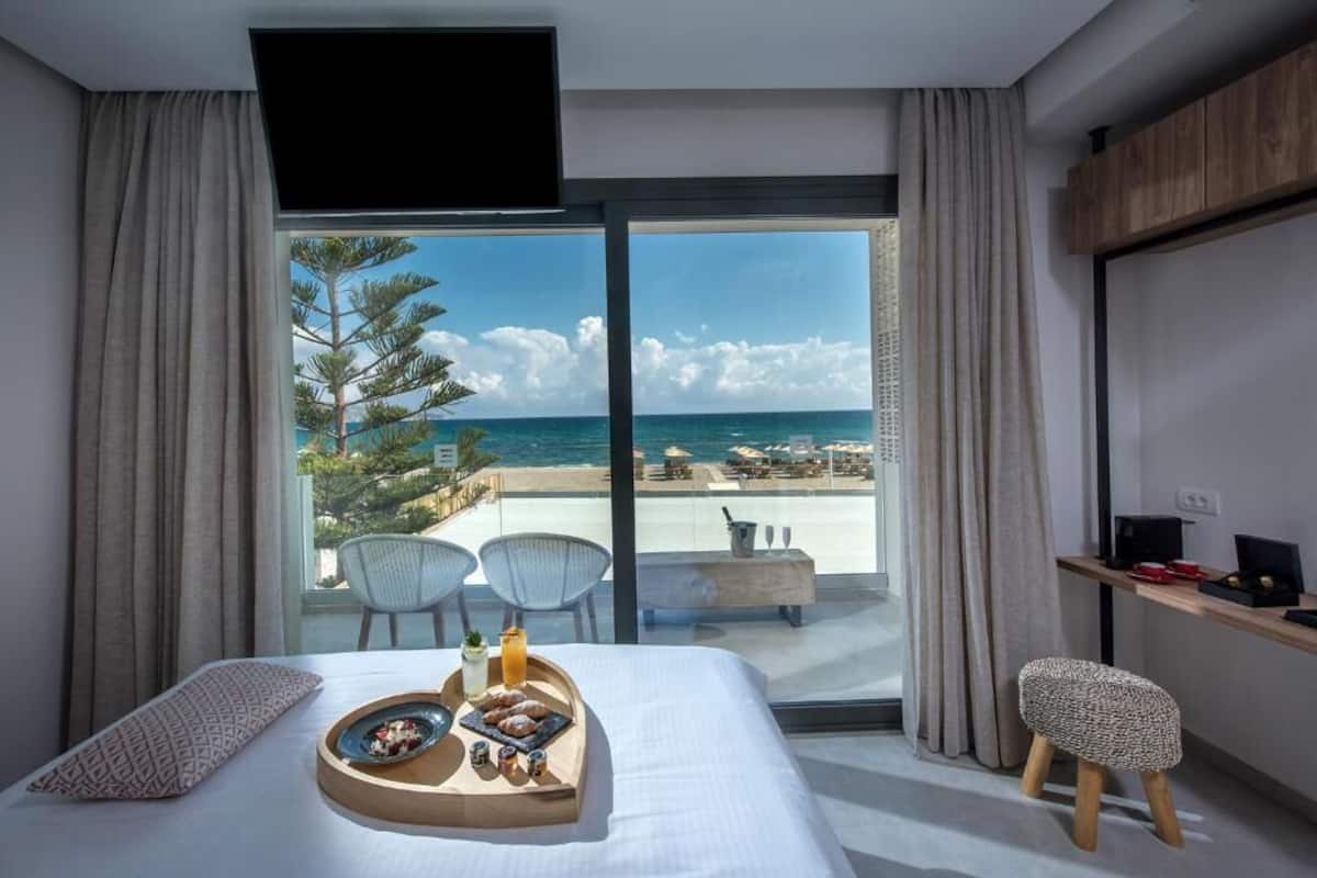 Ein Hotelzimmer mit Bett, Frühstückswagen, Fernseher, Schreibtisch und Blick aufs Meer.