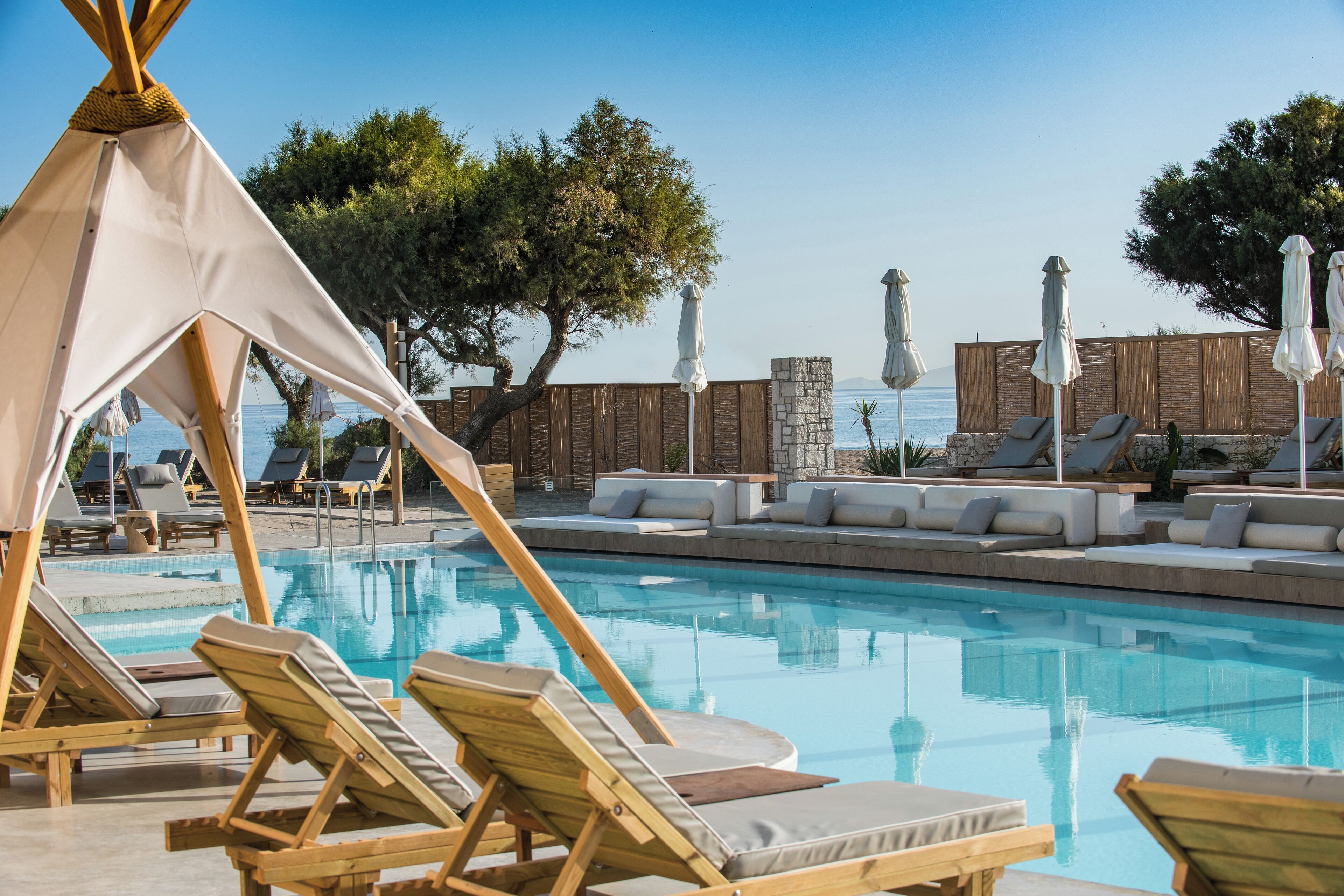 A pool area with wooden loungers, a tent, and a stone wall.