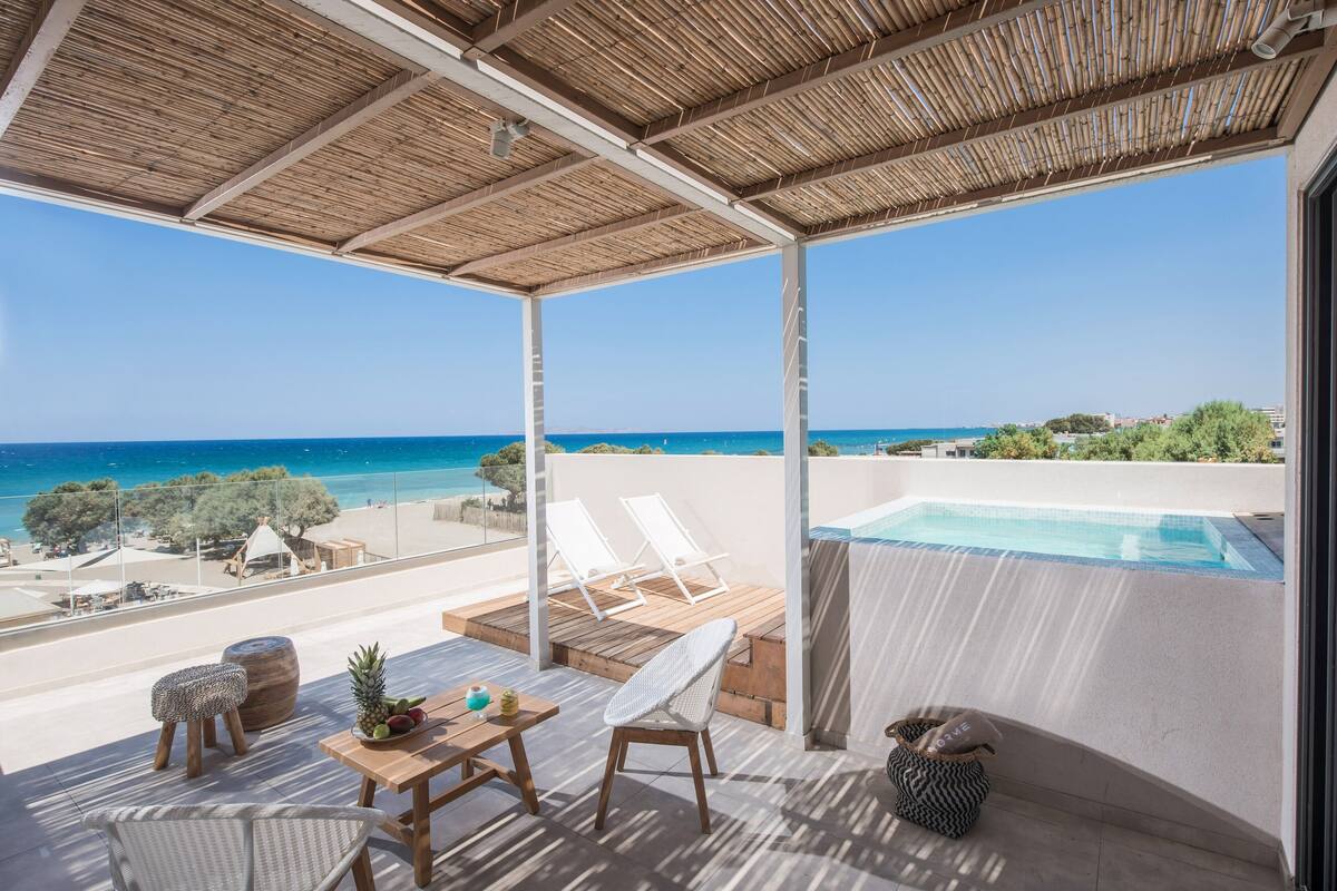 Ein Balkon mit Pool, weißen Stühlen, einem Tisch und Blick aufs Meer.