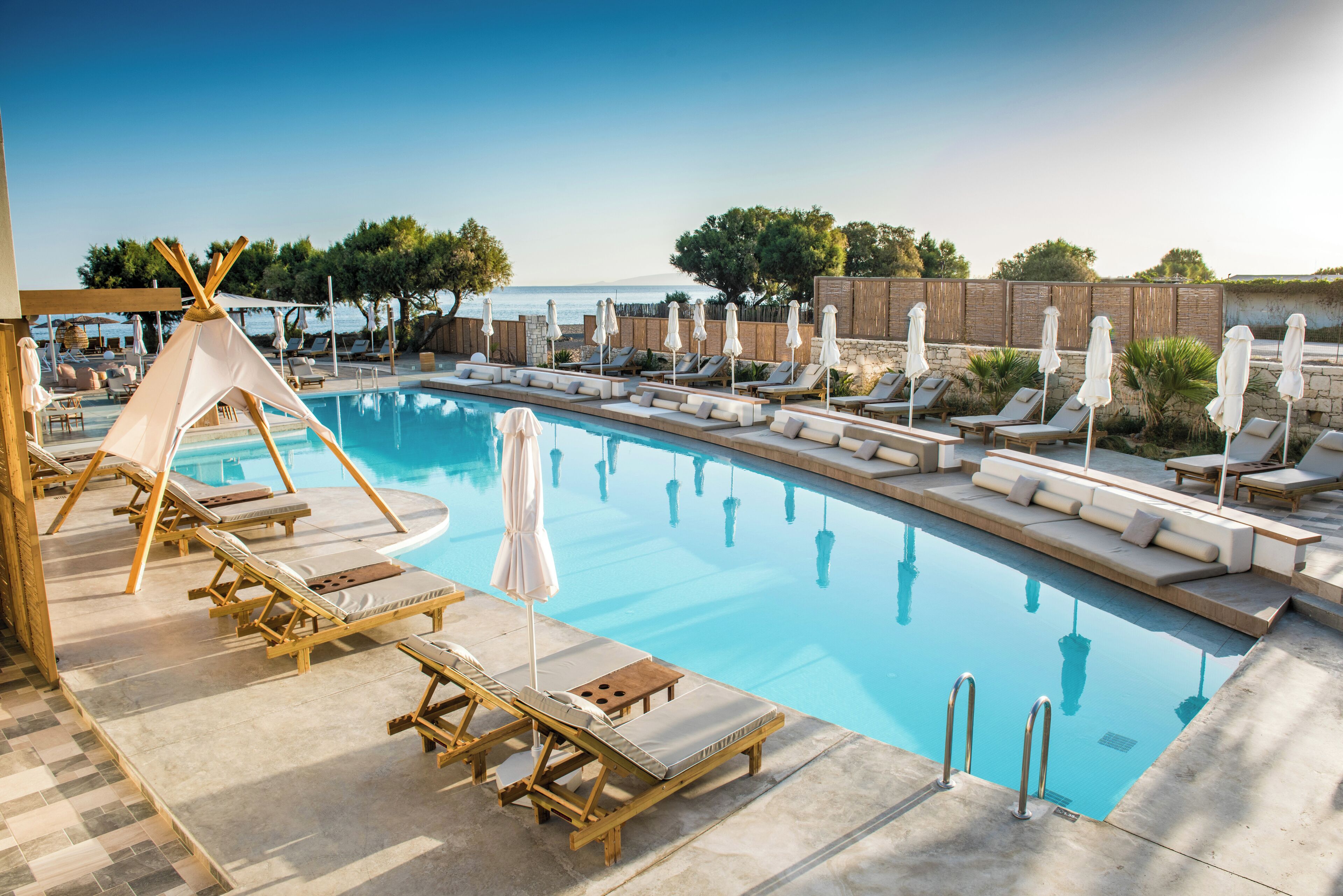 A pool area with lounge chairs and umbrellas, a wooden deck, and a view of the sea.