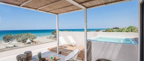 A balcony with a pool, white lounge chairs, and a table with fruit.