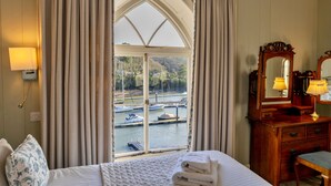 A hotel room with a large bay window, a wooden dresser with a mirror, and a bed with a white comforter. - Captain's Cottage at Mixtow Creek (Lanteglos)