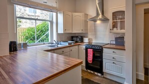 A modern kitchen with white cabinetry, a stainless steel range hood, and a window with a view of greenery. - Captain's Cottage at Mixtow Creek (Lanteglos)