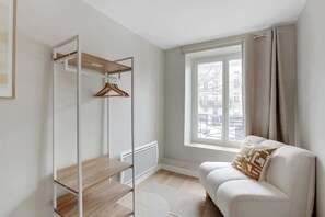 Ein modernes, minimalistisches Zimmer mit einem weißen Sofa, einer Holzregaleinheit und einem großen Fenster mit Vorhängen.