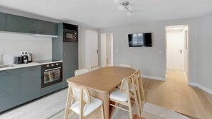 Una cocina moderna con gabinetes grises, una mesa de comedor de madera y un televisor montado en la pared.