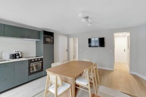 Eine moderne Küche mit grauen Schränken, einem Holzespeise Tisch und einem an der Wand montierten Fernseher.