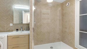 Un baño con lavamanos blanco, un espejo, zona de ducha y una ventana.